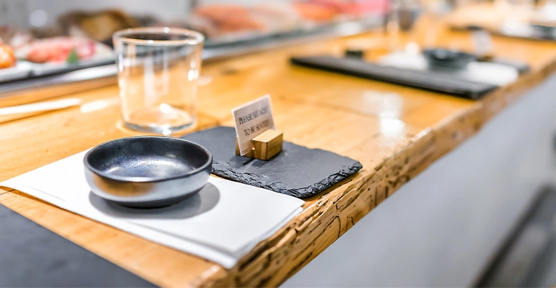 Japanese restaurant sign in traditional style, interior asian sushi wooden bar counter, menu, bowl, glass, napkin setting