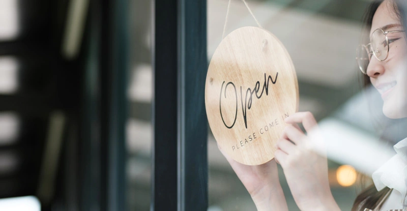 Shopkeeper flipping an open sign at the storefront, signaling the start of the business day.