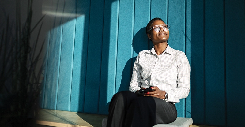 Young adult black woman sitting at office, smiling and relaxing in the sun