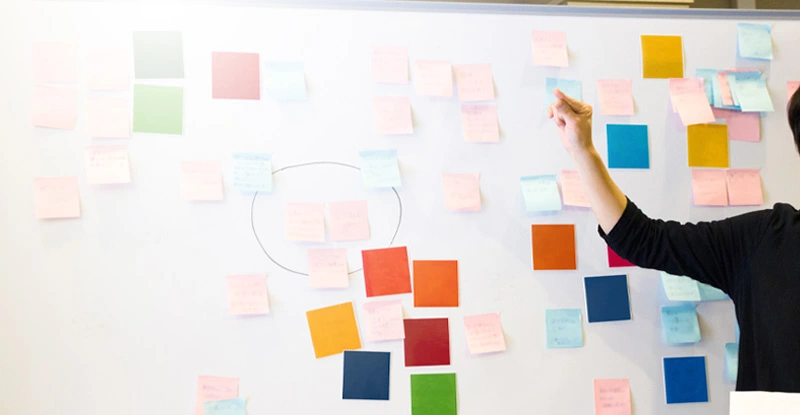Asian female entrepreneur sticks the ideas on adhesive note written by coworkers onto the whiteboard.